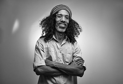 African Rastafarian male smiles and looks at the camera standing with his arms crossed.